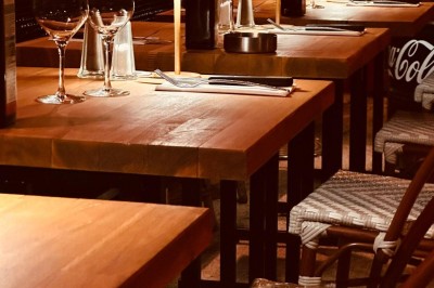 Salle de restaurant lumineuse avec tables en bois, chaises vertes, décorations végétales et comptoir en arrière-plan.