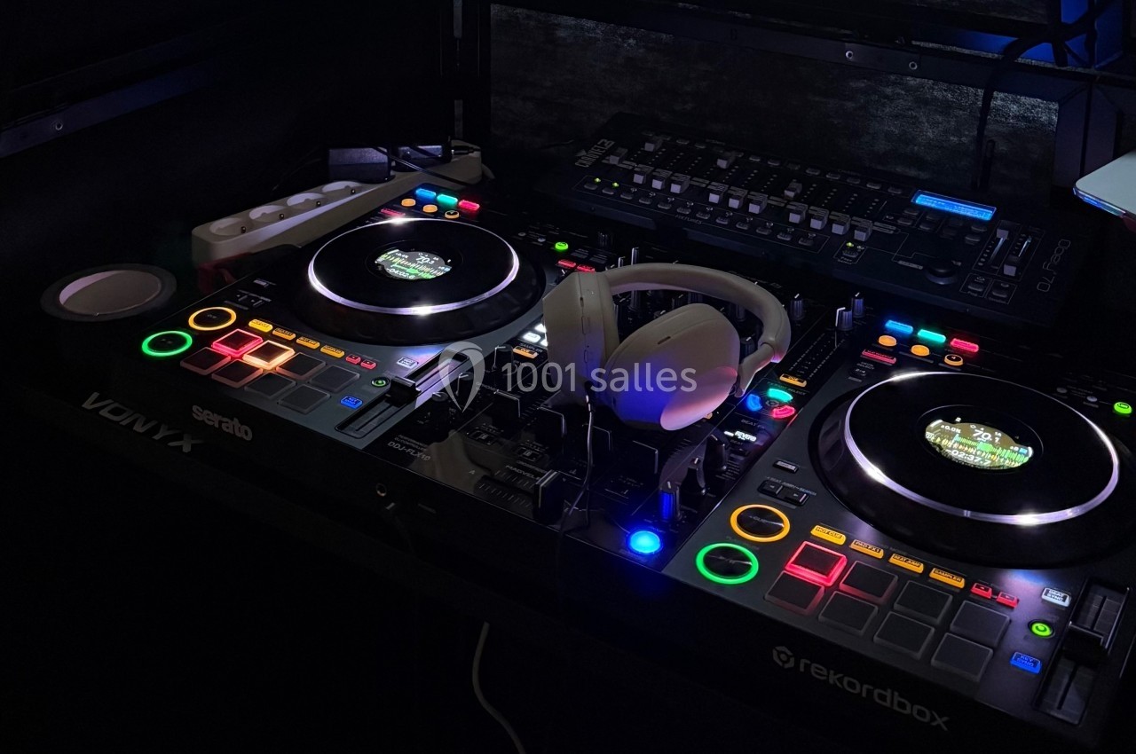 Table de mixage DJ éclairée avec des platines, des boutons colorés et un casque posé au centre.