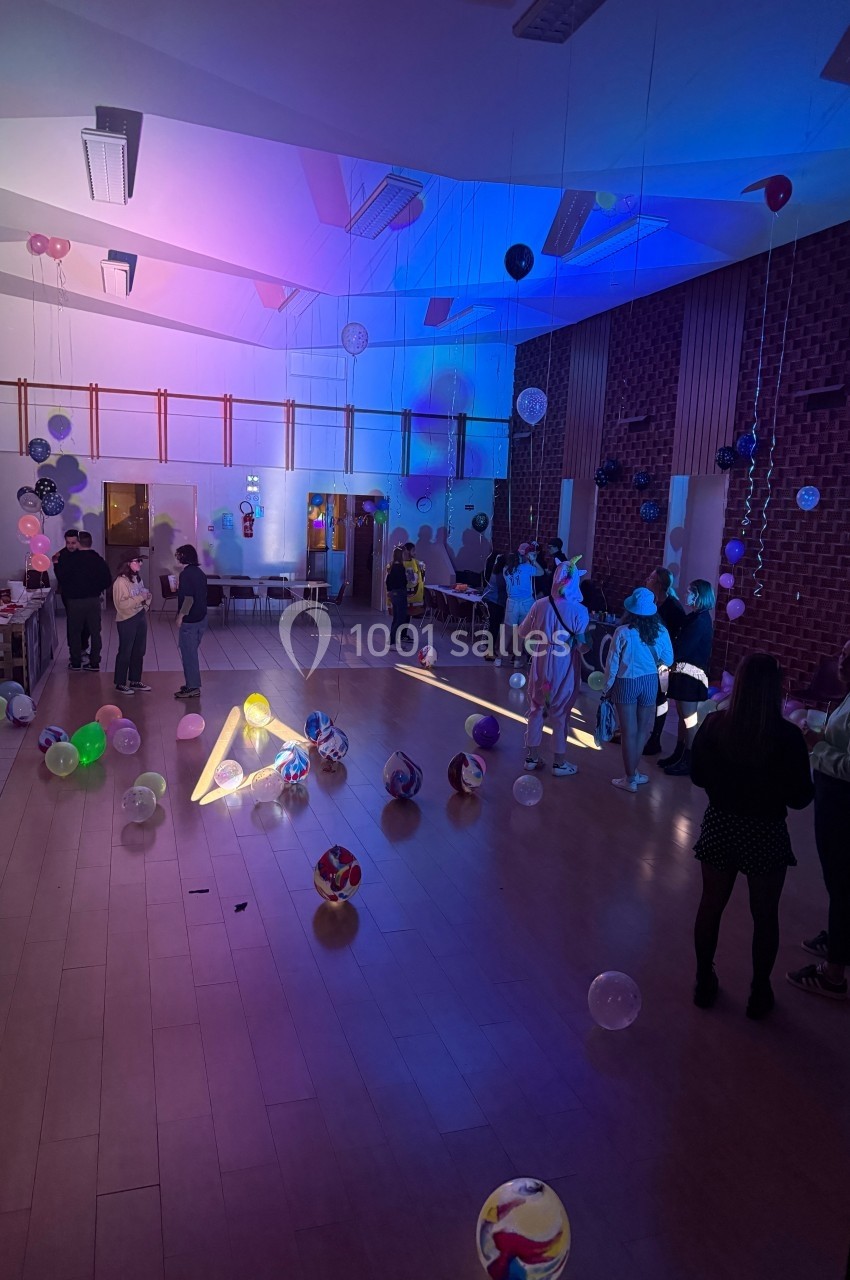 Salle décorée avec des ballons lumineux, éclairée par des lumières colorées, avec des personnes discutant et se déplaçant.