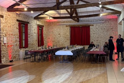 Salle de réception avec murs en pierre, poutres apparentes, tables dressées et éclairage tamisé.