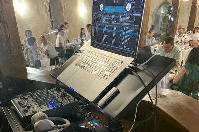 Poste de DJ avec ordinateur portable et table de mixage, en arrière-plan des convives assis dans une salle de réception.