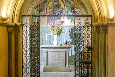 Statue de sphinx en pierre posée sur un socle, entourée de végétation et d'une haie dans un jardin.