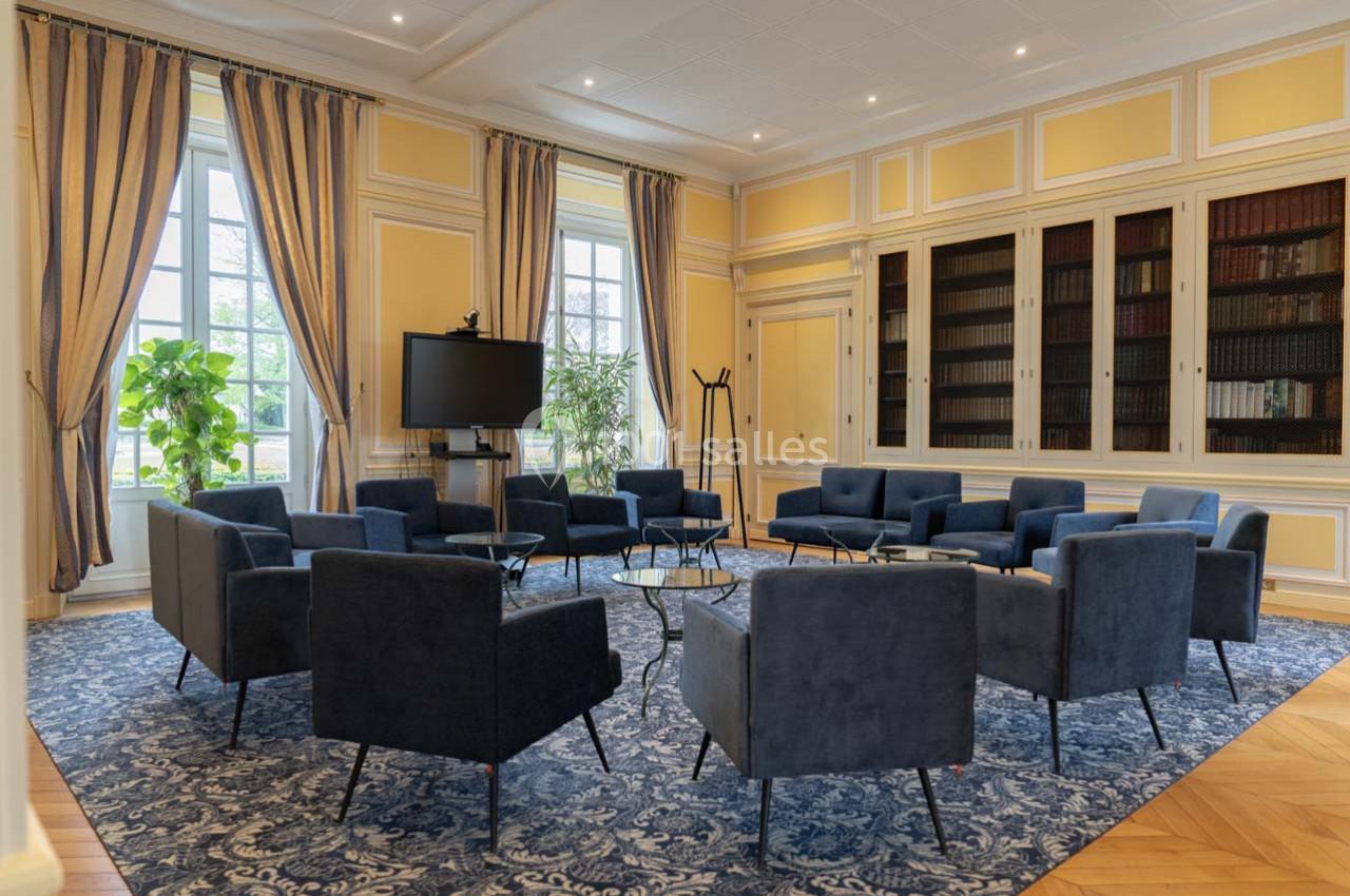 Salle de réunion lumineuse avec fauteuils bleus disposés en cercle, bibliothèque en arrière-plan et écran de présentation.