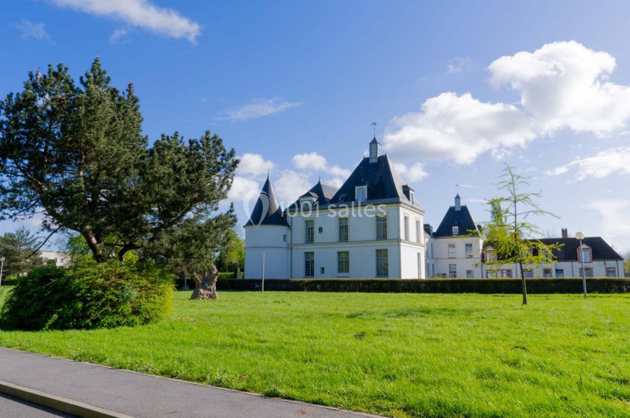 Château blanc entouré de verdure avec un ciel bleu et quelques nuages en arrière-plan.