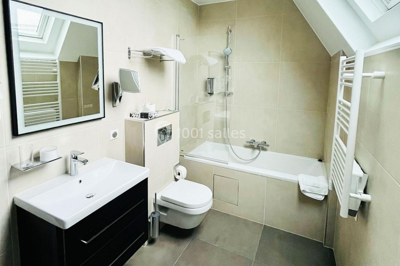 Salle de bain moderne avec baignoire, lavabo, toilettes suspendues, miroir et porte-serviettes chauffant.