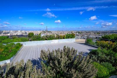 Vue d'une terrasse végétalisée surplombant Paris avec la Tour Eiffel visible à l'horizon sous un ciel bleu.