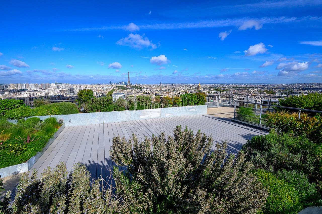 Vue d'une terrasse végétalisée surplombant Paris avec la Tour Eiffel visible à l'horizon sous un ciel bleu.