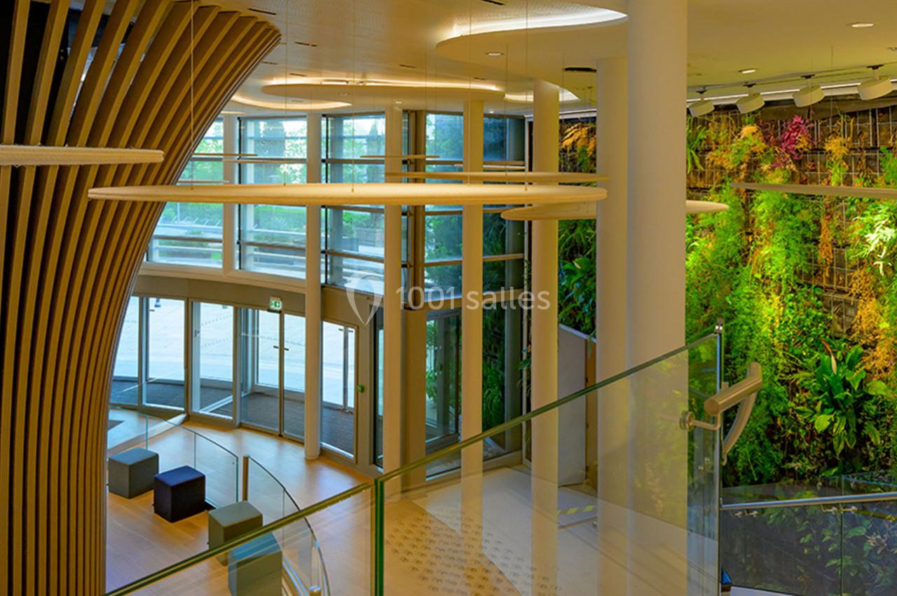 Entrée lumineuse avec des murs végétalisés, des sièges modernes et une structure en bois incurvée.