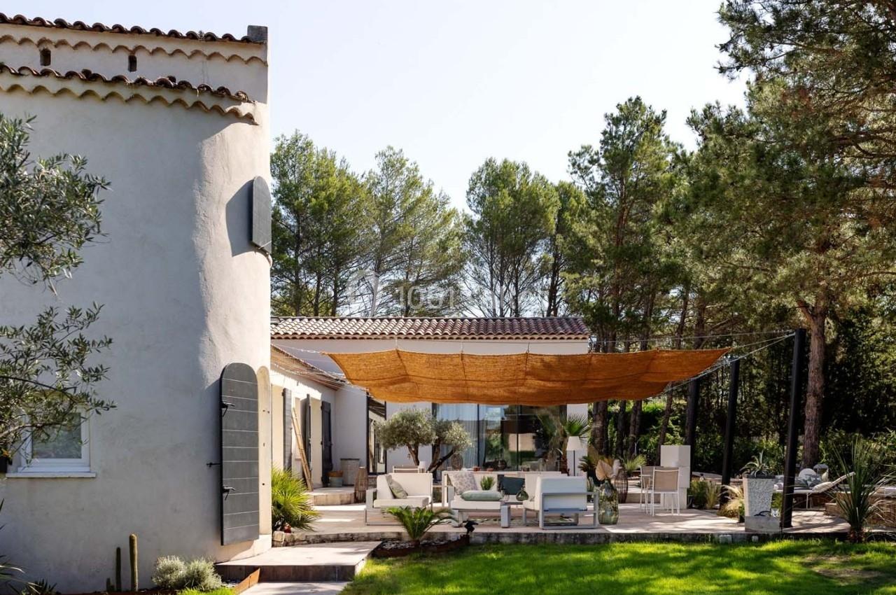 Terrasse aménagée avec voiles d'ombrage, mobilier extérieur et jardin arboré, attenante à une maison en pierre.
