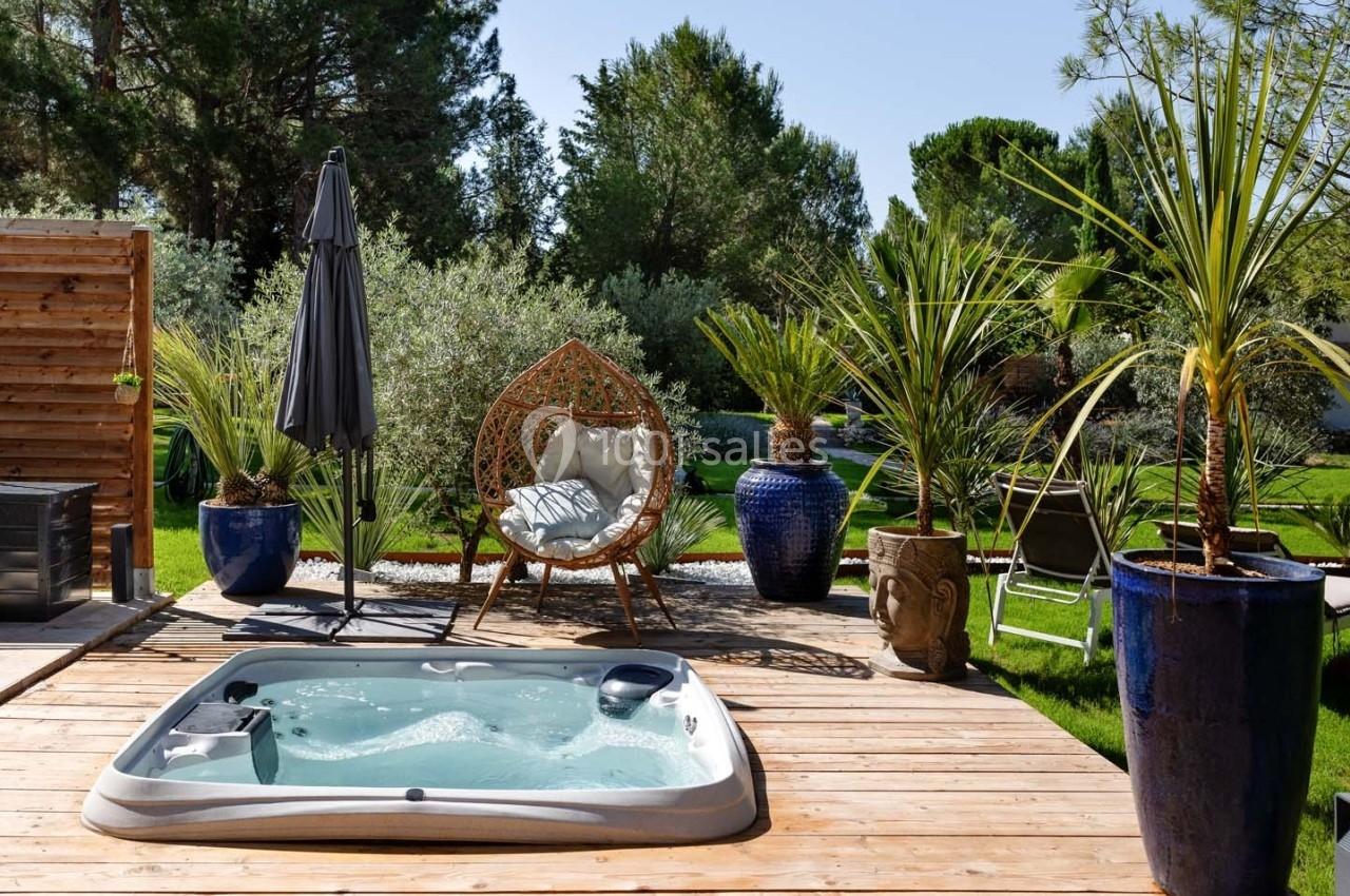 Jacuzzi encastré sur une terrasse en bois, entouré de plantes en pot et de mobilier de jardin sous un ciel dégagé.