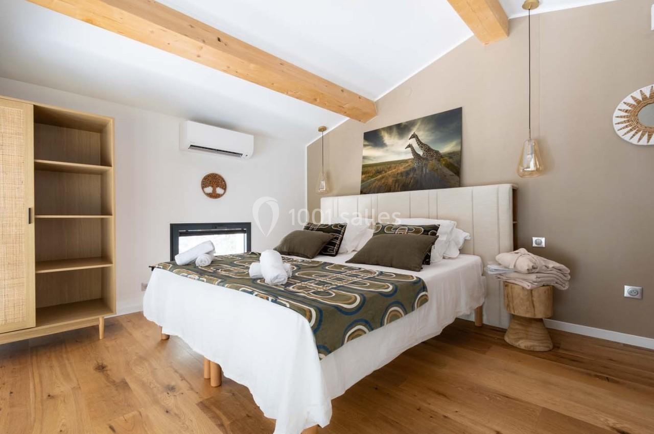 Chambre lumineuse avec lit double, décoration naturelle, poutres apparentes et mobilier en bois clair.