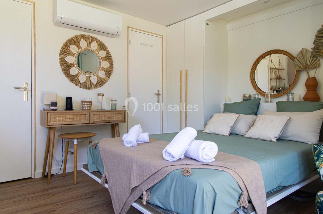 Chambre lumineuse avec lit double, linge plié, bureau en bois, miroir décoratif et climatisation murale.