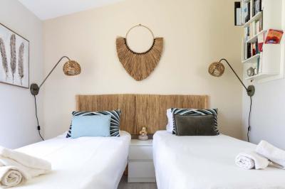 Deux lits simples avec linge blanc, coussins décoratifs, lampes murales et décoration murale en fibres naturelles.