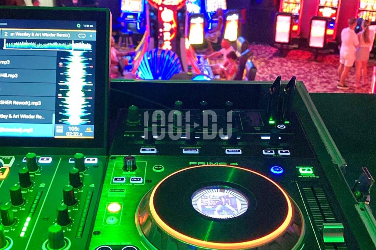 Console DJ allumée avec platines et écran, située dans un espace lumineux avec des machines de jeu en arrière-plan.