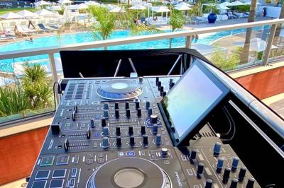 Console de DJ avec enceintes sur une terrasse en hauteur, offrant une vue sur la mer et des bâtiments en arrière-plan.