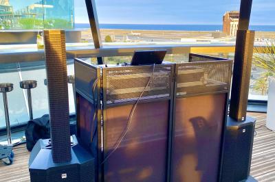 Console de DJ avec enceintes sur une terrasse en hauteur, offrant une vue sur la mer et des bâtiments en arrière-plan.