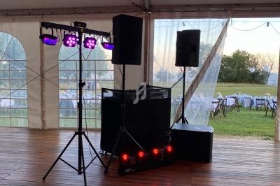 Équipement de sonorisation et éclairage installé sous une tente, avec des tables dressées en extérieur en arrière-plan.