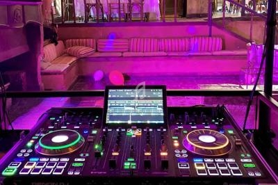 Table de mixage DJ illuminée avec des contrôles et un écran, installée dans un espace intérieur avec des sièges en arrière…