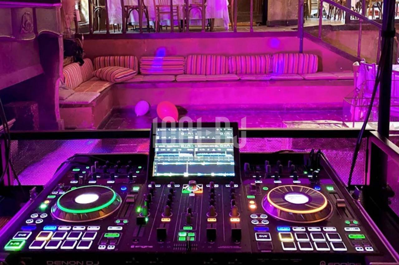 Table de mixage DJ illuminée avec des contrôles et un écran, installée dans un espace intérieur avec des sièges en arrière…