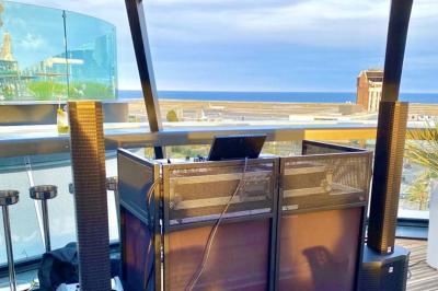 Console de DJ avec enceintes sur une terrasse en hauteur, offrant une vue sur la mer et des bâtiments en arrière-plan.