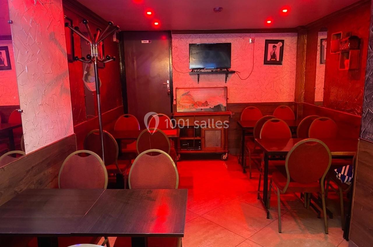 Salle de restaurant avec des tables et chaises alignées, éclairée par une lumière rouge et une télévision fixée au mur.