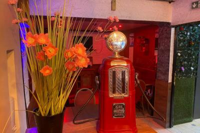 Façade d'un café avec une table extérieure en bois, revêtement en gazon synthétique et intérieur éclairé visible.