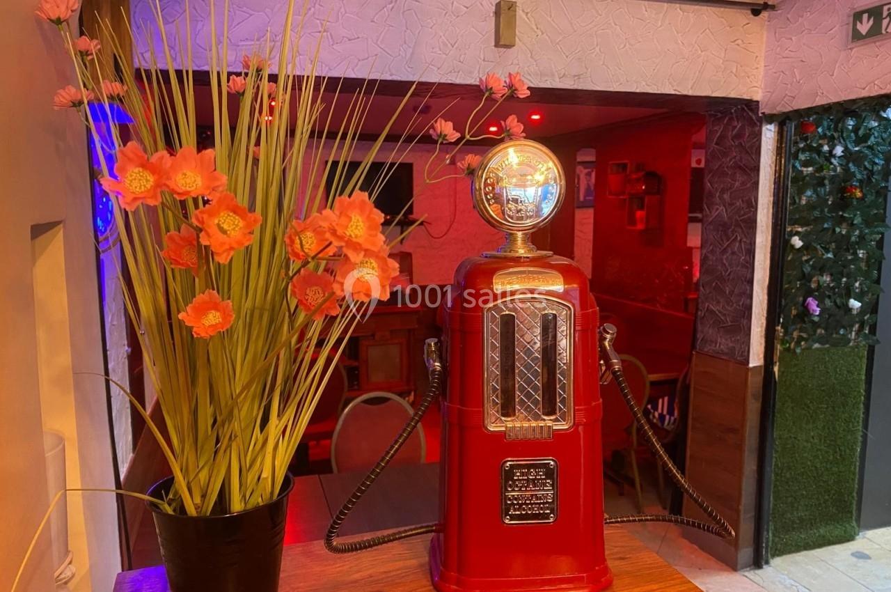 Pompe à essence vintage rouge décorative sur une table en bois, accompagnée d'un vase de fleurs orange.