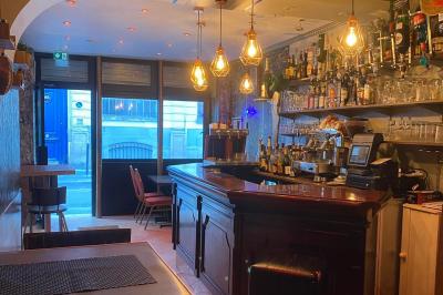 Façade d'un café avec une table extérieure en bois, revêtement en gazon synthétique et intérieur éclairé visible.