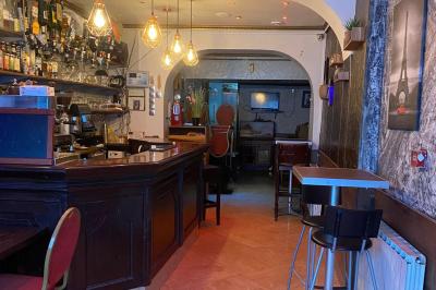Façade d'un café avec une table extérieure en bois, revêtement en gazon synthétique et intérieur éclairé visible.