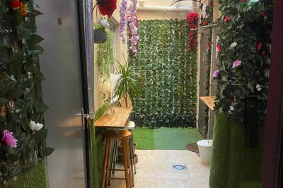 Façade d'un café avec une table extérieure en bois, revêtement en gazon synthétique et intérieur éclairé visible.
