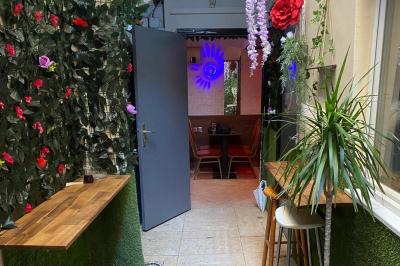 Façade d'un café avec une table extérieure en bois, revêtement en gazon synthétique et intérieur éclairé visible.