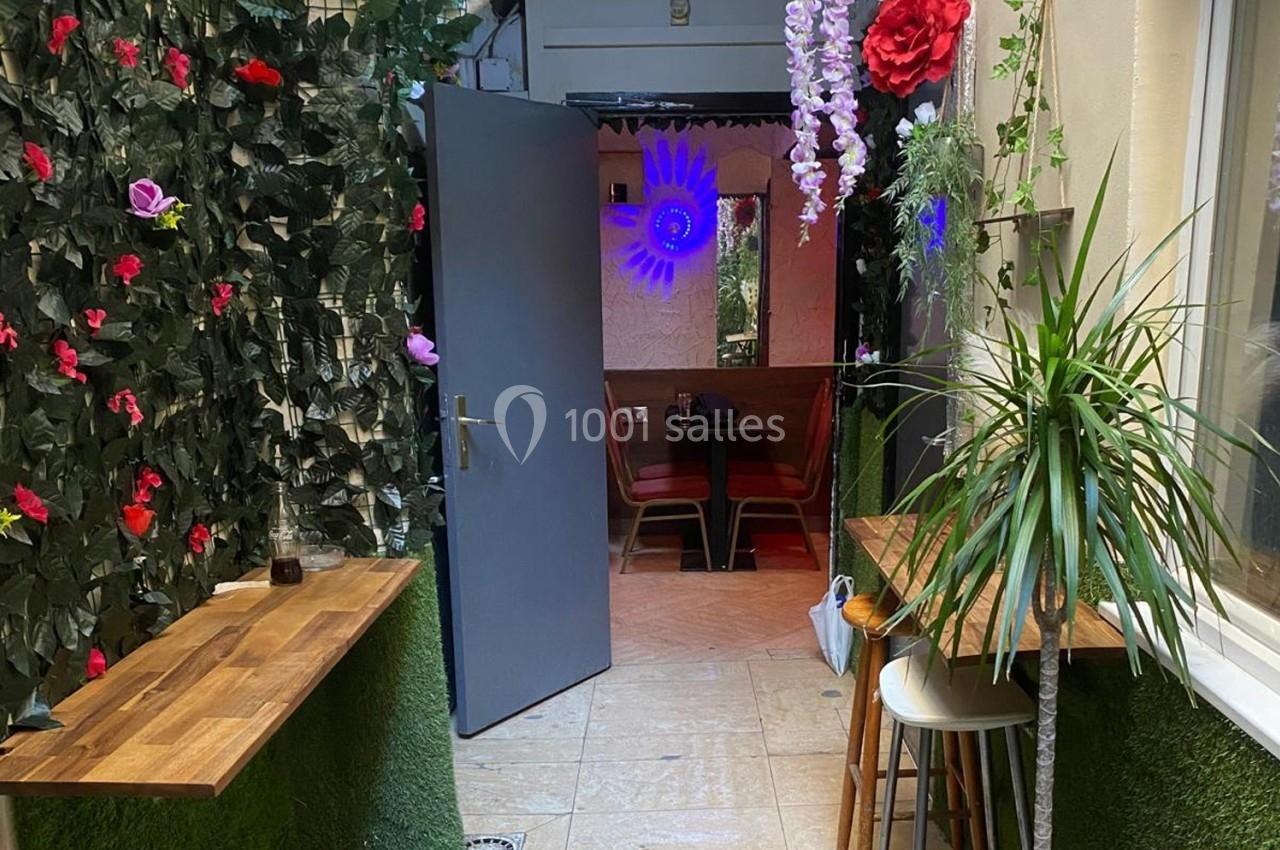 Entrée d'un espace intérieur avec plantes décoratives, tables en bois et lumière colorée en arrière-plan.