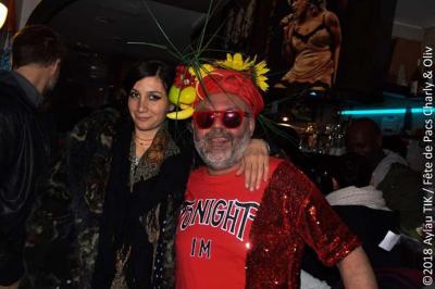 Façade d'un café avec une table extérieure en bois, revêtement en gazon synthétique et intérieur éclairé visible.