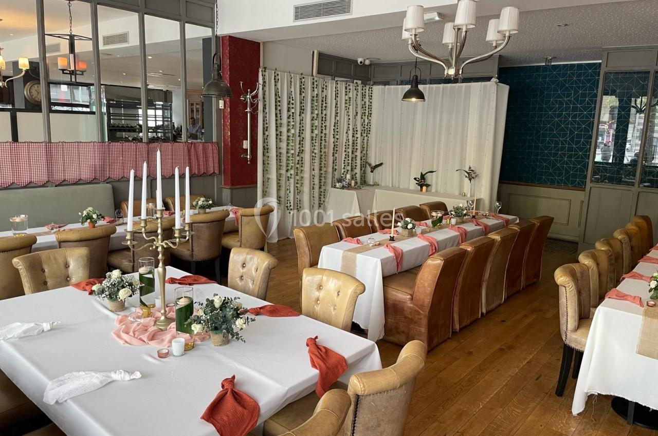 Salle de restaurant décorée pour un événement, avec tables dressées, nappes blanches et éléments floraux.