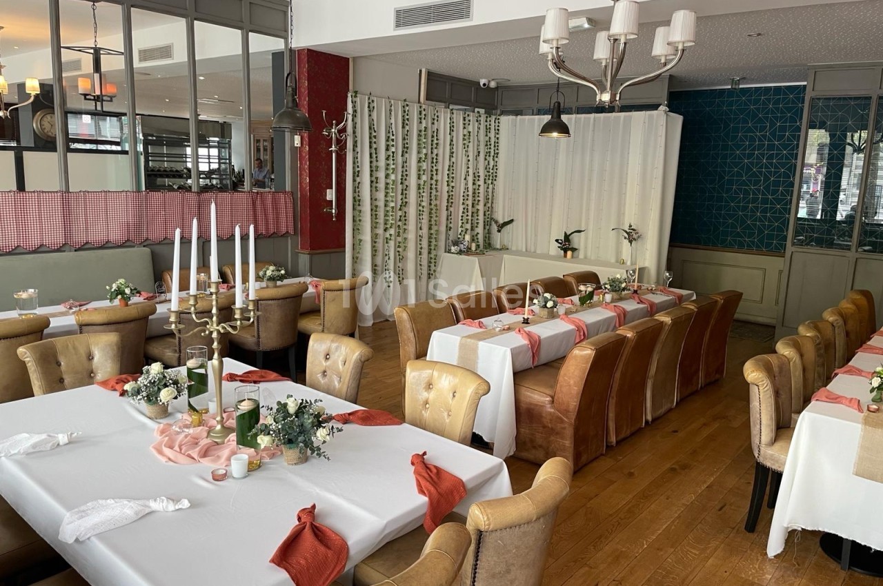 Salle de restaurant décorée pour un événement, avec tables dressées, nappes blanches et éléments floraux.