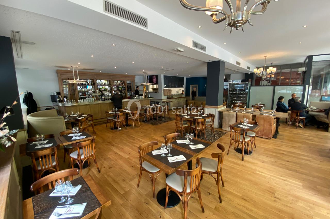 Salle de restaurant lumineuse avec tables en bois, chaises assorties et un bar en arrière-plan.