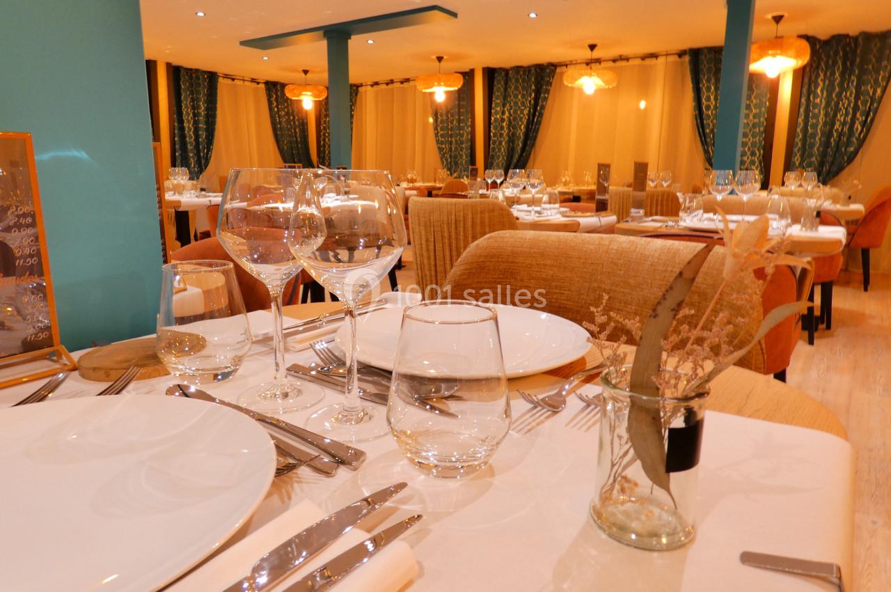 Salle de restaurant élégante avec tables dressées, nappes blanches, verres et chaises en bois, éclairage chaleureux.