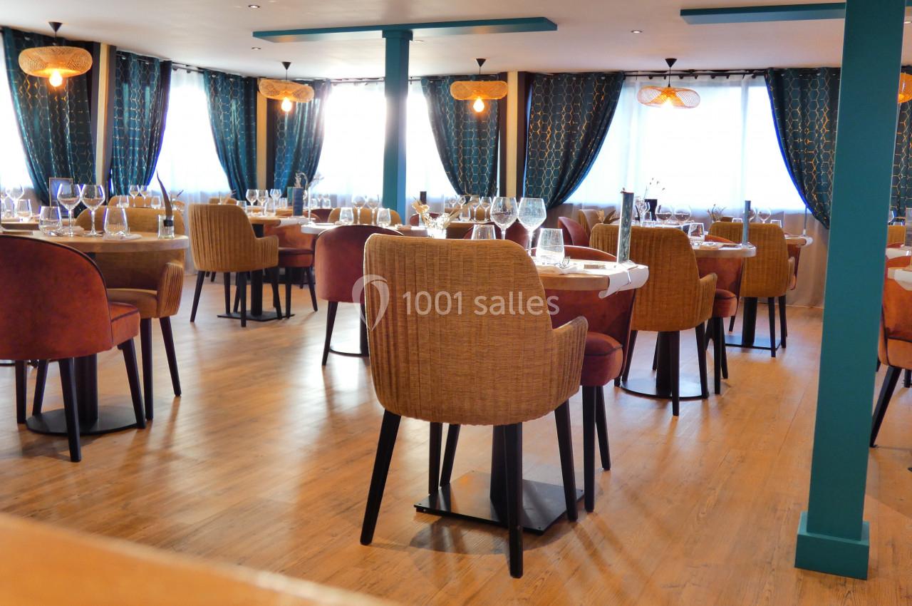 Salle de restaurant lumineuse avec tables dressées, chaises en tissu et rideaux sombres ornés de motifs dorés.