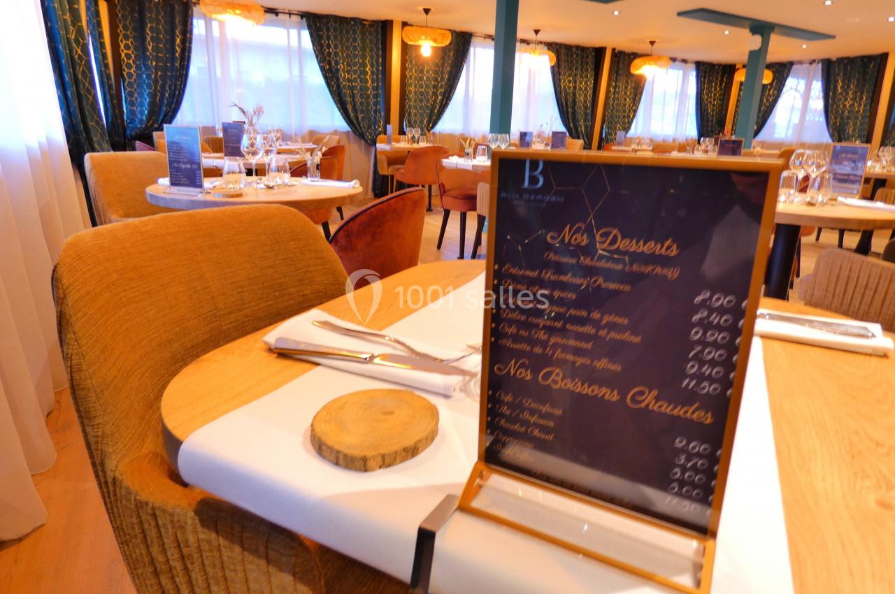 Carte des desserts posée sur une table dressée dans un restaurant élégant avec rideaux et éclairage chaleureux.