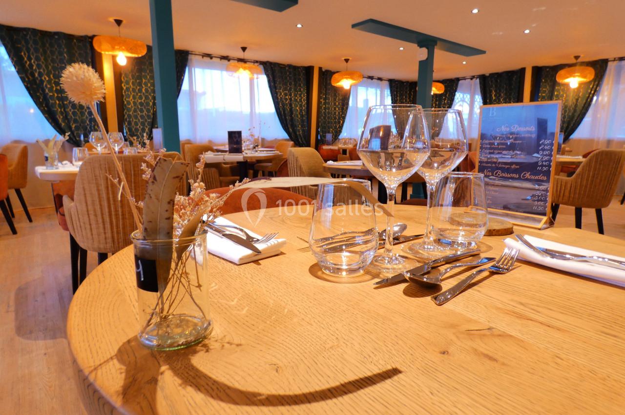 Salle de restaurant élégante avec table dressée, verres, couverts et décoration florale, éclairée par des suspensions.