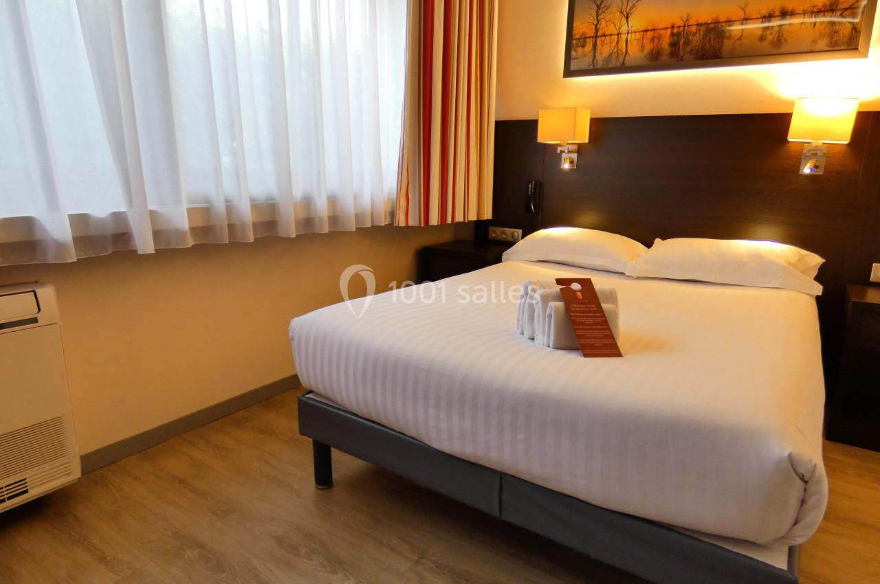 Chambre d'hôtel avec lit double, draps blancs, éclairage chaleureux, grande fenêtre et tableau mural.