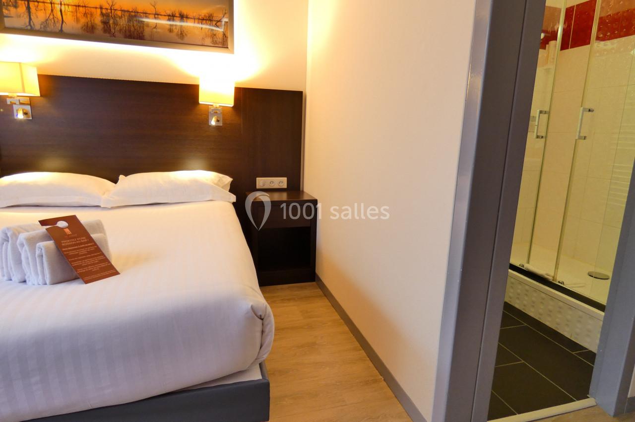 Chambre d'hôtel avec lit double, table de chevet, éclairage mural et salle de bain attenante avec douche.