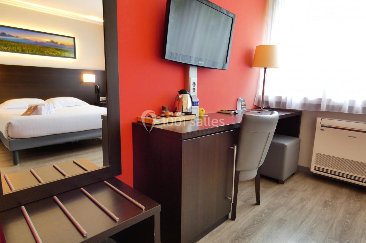 Chambre d'hôtel avec lit double, bureau, télévision murale, plateau de courtoisie et grande fenêtre laissant entrer la…