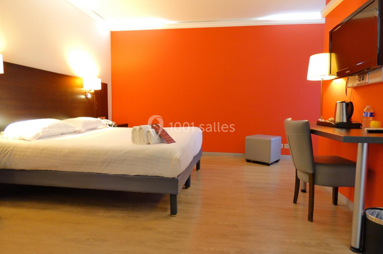 Chambre d'hôtel avec lit double, bureau, télévision murale, lampe et mur rouge vif en arrière-plan.