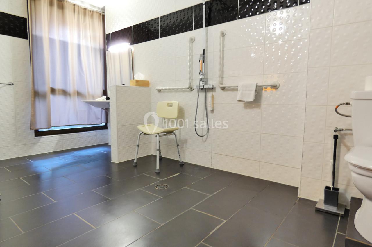 Salle de bain accessible avec douche à l'italienne, chaise de douche, barres d'appui et carrelage clair.