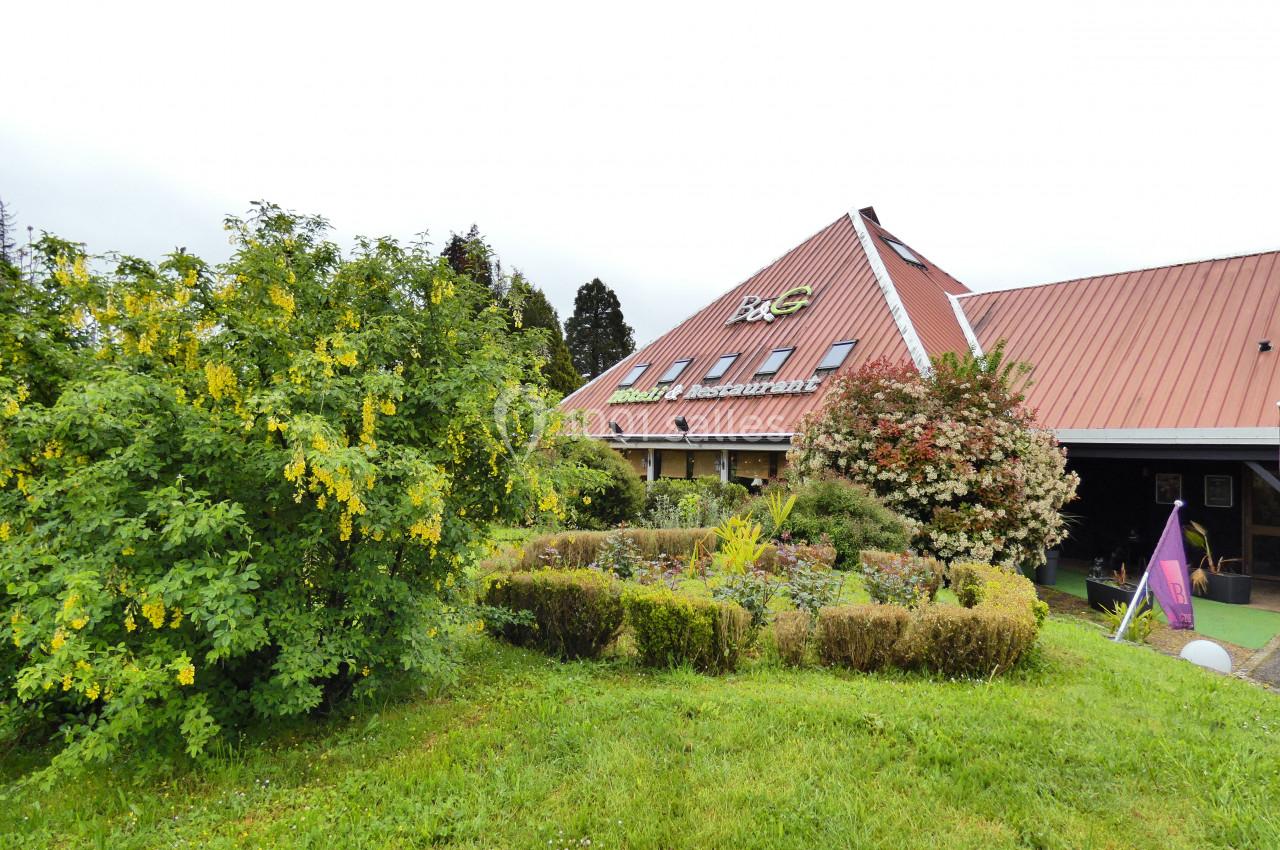 Façade d'un restaurant avec un toit en pente, entouré de verdure et d'arbustes fleuris.