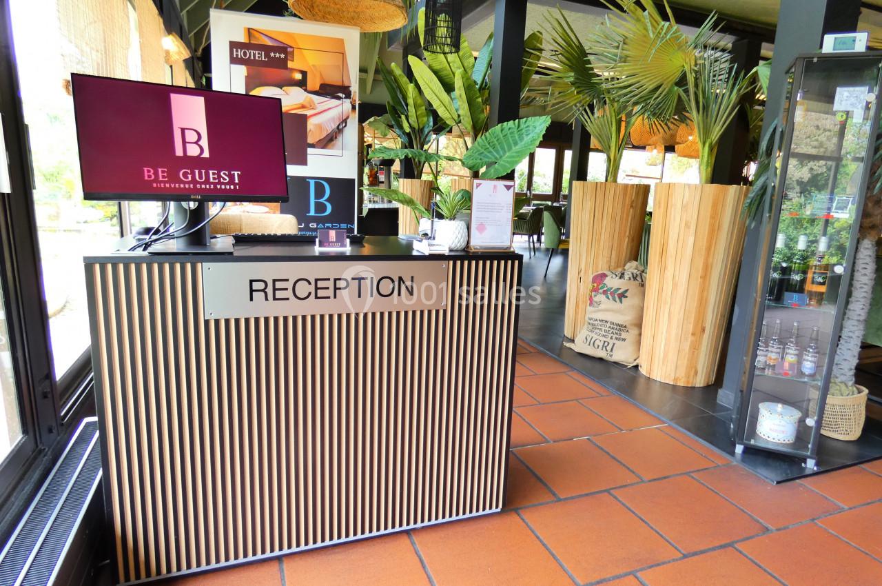 Comptoir de réception moderne avec écran allumé, plantes décoratives et lumière naturelle en arrière-plan.