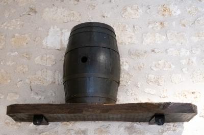 Barbecue en métal rouillé posé sur un socle en pierre, entouré de végétation et de murs en pierre.