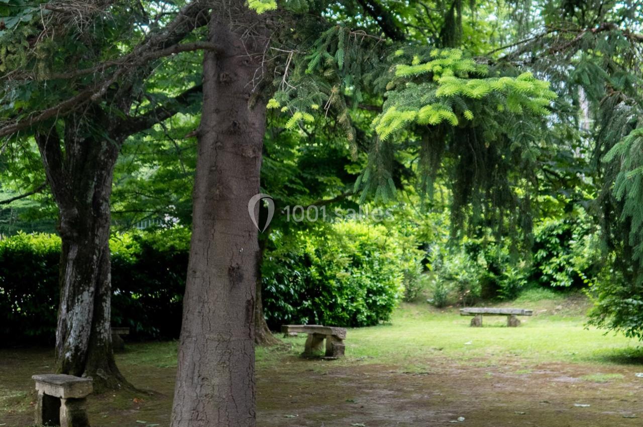 Un petit espace vert ombragé avec des bancs en pierre entourés d'arbres et de buissons.