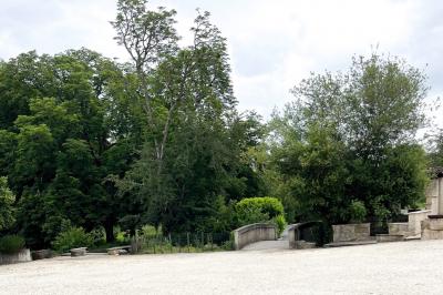 Barbecue en métal rouillé posé sur un socle en pierre, entouré de végétation et de murs en pierre.